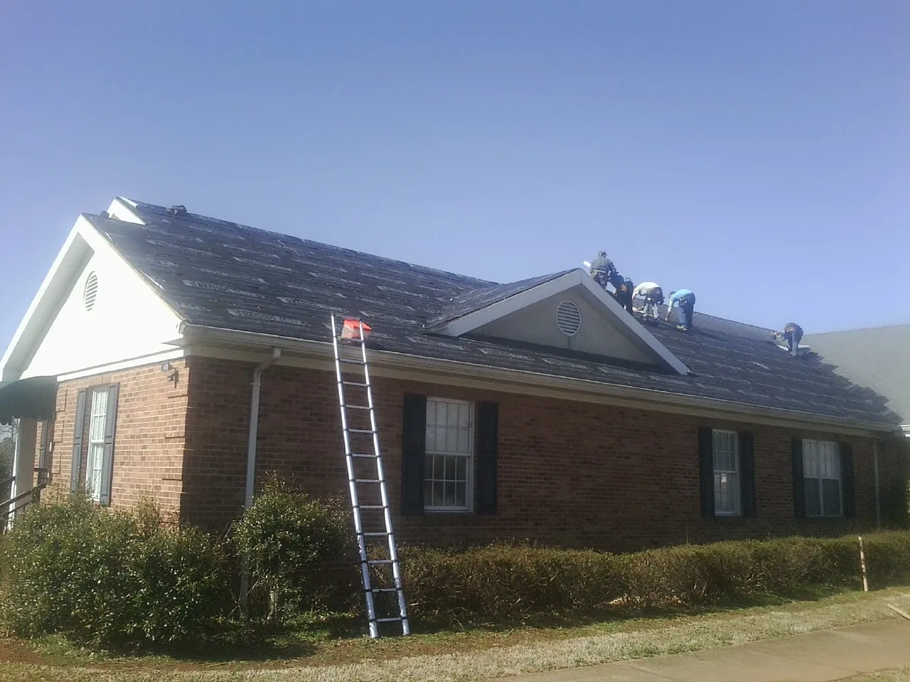 Crew tearing shingles off a brick ranch roof with a ladder set — Emergency Roof Repair work by our crew in Redfield