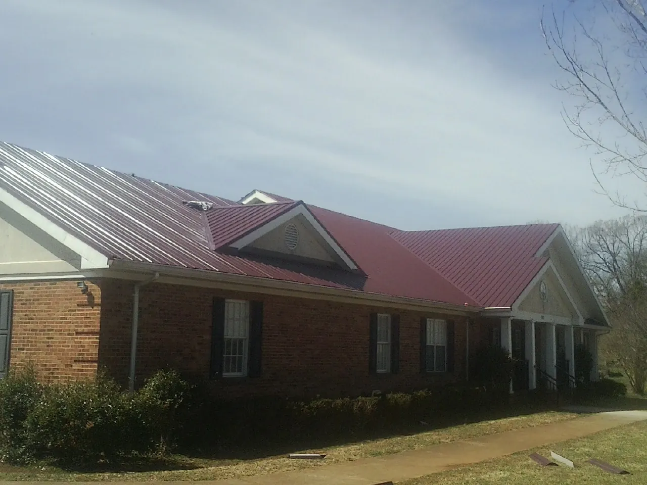 Red metal roof with gabled entries on a long brick building, from a Hail Damage Roof Repair job in Redfield